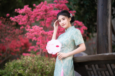 穿旗袍的女子拿着扇子站在亭子旁