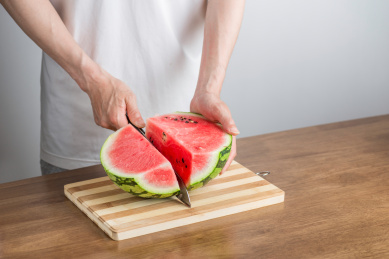 手拿三德刀在拼竹砧板上切西瓜