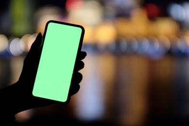 手展示绿色屏幕的手机和夜晚多彩的城市光斑