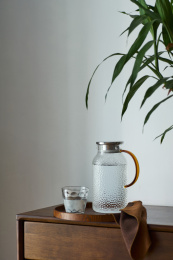 圆形松木托盘里的锤纹玻璃凉水壶和水杯