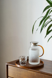 圆形松木托盘里的锤纹玻璃凉水壶和水杯