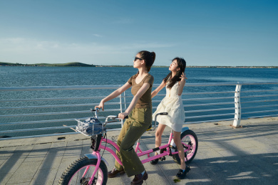 夕阳下湖边码头骑双人脚踏车的闺蜜少女