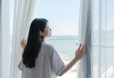 女人站在窗边手拉开窗帘，她看着窗外的海景