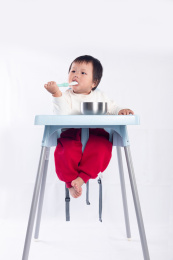 坐在餐桌上的宝宝手拿勺子把食物送进嘴里