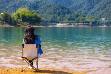 一个女人在水边坐在一把折叠椅上