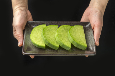 手端一盘青萝卜片特写黑色背景