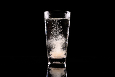 黑色背景中维生素C泡腾片在比玻璃杯中融化