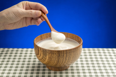 女性手用勺子盛酸奶特写格子桌布背景