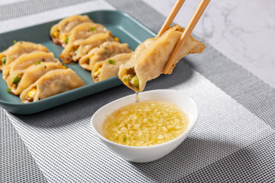 夹在筷子上的大肉锅贴蘸蒜汁