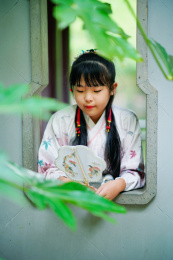 身穿汉服的女孩手持蒲扇在窗台前静思