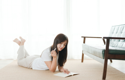 美女趴在地毯上拿着笔准备在本子上书写