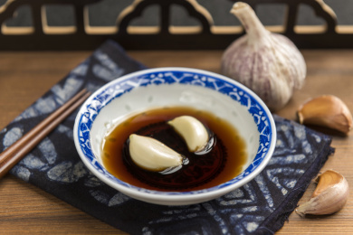 泡着大蒜瓣的醋碟摆放在木桌面上特写