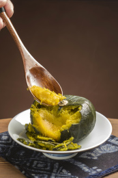 一盘蒸南瓜摆放在木桌面上勺盛蒸南瓜特写