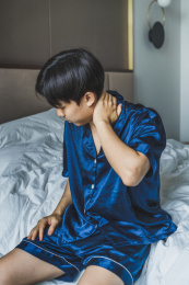 亚洲男子坐在床边扶住脖子