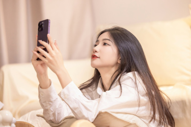 一位年轻女性坐在沙发旁玩手机自拍打哈欠