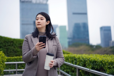年轻的职业女性在旅途中使用智能手机和咖啡