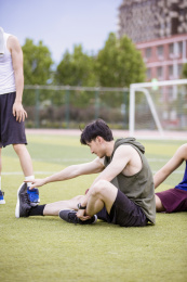 青年男子在学校足球场做拉伸运动准备打篮球