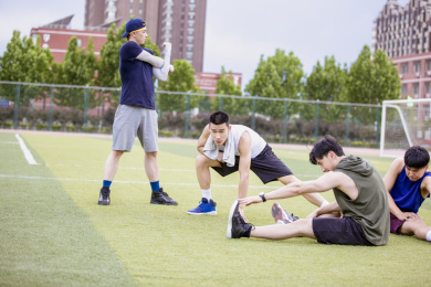 四个青年男子在足球场做拉伸运动准备打篮球