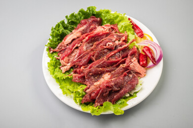 白色桌面上有一盘生制炒烤牛肉切片