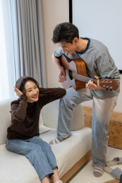 一对年轻情侣坐在沙发上弹吉他