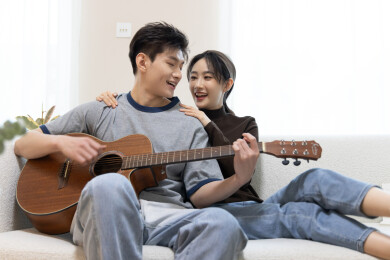 一对年轻情侣坐在沙发上弹吉他
