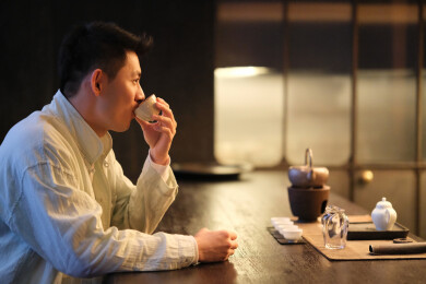一位年轻中国男人拿着茶杯在茶馆喝茶