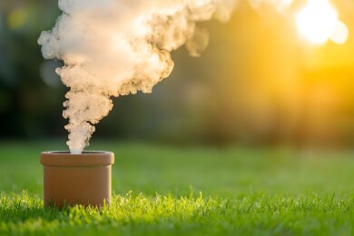 烟囱上升起的白烟与阳光下的山丘