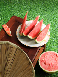 夏天绿色草坪上摆放着的新鲜水果西瓜和蒲扇