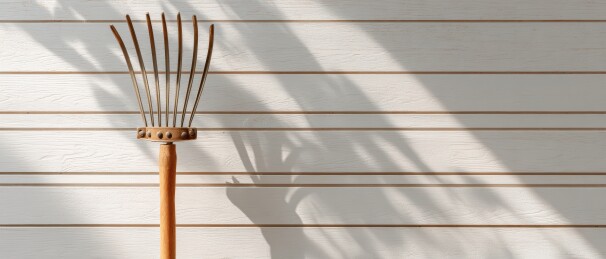 木制耙子倚靠在白色木板墙上的静物光影