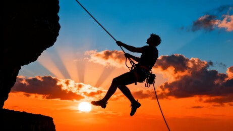 夕阳下攀岩者悬空绳降剪影