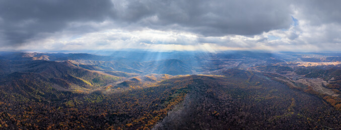 阳光穿过云层洒向山脉与秋日森林全景