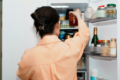 女人从冰箱货架上取食物罐头