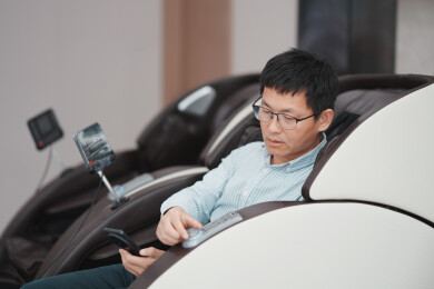 戴眼镜男子坐按摩椅操作手机遥控器