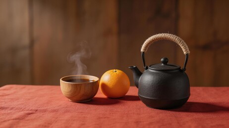 木质茶杯热气升腾旁置橙子与铁壶