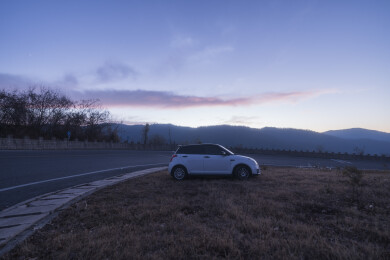 黄昏时分停在山路边草地上的白色小型汽车
