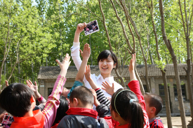 女教师与佩戴红领巾的学生在树林中开心合影