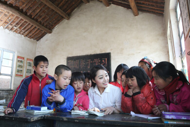 乡村小学女教师与多名学生在课桌前辅导功课