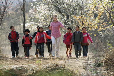 女教师带领一群小学生在开满花的路上行走