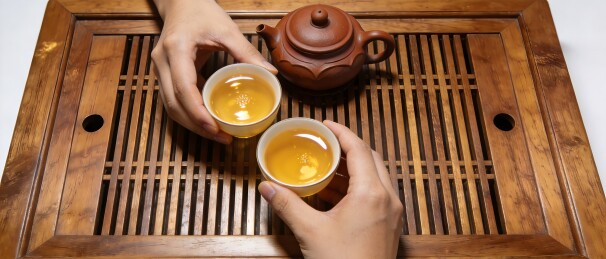 双手捧茶杯木质茶盘上