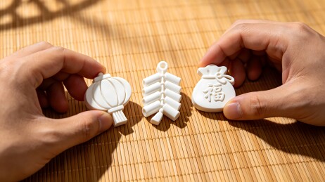 双手分别拿着三个白色的小物件，分别是灯笼、元宝和钱袋